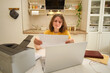 © Андрей Журавлев - A woman with a laptop prints paper on a printer while sitting at a table in a home kitchen. An adult female businesswoman works from home