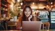 © CraftyImago - Young Asian woman using laptop working at a coffee shop happy and smile.