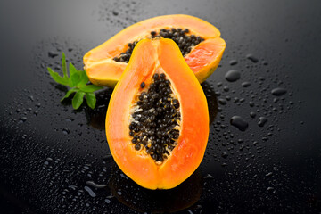 Wall Mural - Papaya fruit on wet black background with water drops. Halved fresh organic Papaya exotic fruits with leaf close up. Healthy vegan food 