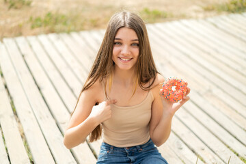 Wall Mural - Teenager girl holding a donut at outdoors with surprise facial expression