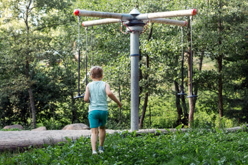 Wall Mural - A little boy in blue clothes, photographed from behind, sees a rope carousel in the forest and rushes towards it