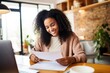 Smiling young black woman sitting at desk working on laptop writing letter in paper notebook, free copy space. Happy millennial female studying using pc. Business And Education Concept