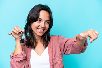 Wall Mural - Young hispanic woman holding home keys isolated on blue background giving a thumbs up gesture