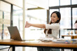 © Wasana - A female employee stretching lazy at the desk to relax while working in the office. Feeling stressed and achy from work.