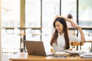 A female employee stretching lazy at the desk to relax while working in the office. Feeling stressed and achy from work.