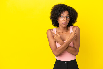 Wall Mural - Young African American woman isolated on yellow background pointing to the laterals having doubts