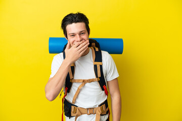 Wall Mural - Young mountaineer Russian man with a big backpack isolated on yellow background happy and smiling covering mouth with hand