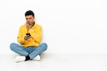 Young African American man sitting on the floor isolated on white background thinking and sending a message