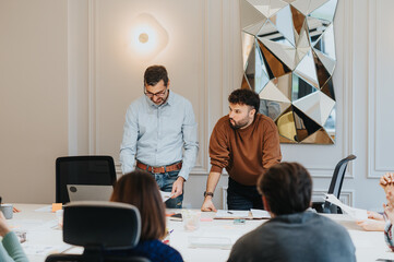 Wall Mural - Two men are actively discussing business matters in a well-lit office with attentive colleagues. The serious ambiance conveys a sense of collaboration.