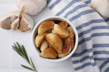 Canvas Print - Fried garlic cloves in bowl and rosemary on table, flat lay