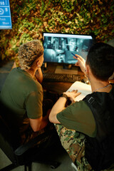 Young confident male officer pointing at computer screen while explaining something to female colleague during surveillance work