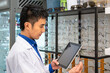 Portrait of young Asian male man optician in optical shop store, holding digital tablet. Eyecare and shopkeeper concept.