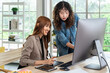 Two smiling young Asian female woman businessperson graphic designer working together, meeting and brainstorming, using computer in office, pointing at screen.