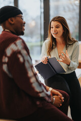 Wall Mural - Two engaged business colleagues in a candid conversation, with a woman holding a notebook and explaining something to her colleague.