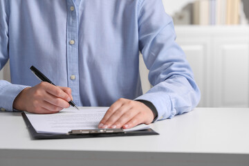 Canvas Print - Woman signing document at white table indoors, closeup. Space for text