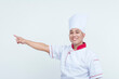 Happy Asian male chef in uniform pointing to the side, isolated on a white background, conveying a friendly gesture.