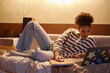 © Seventyfour - Full length portrait of Black teenage girl lying on bed at home and using laptop at night