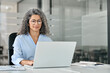 © insta_photos - Busy older middle aged professional business woman manager executive wearing eyeglasses looking at laptop computer working in office managing digital financial banking data sitting at desk.