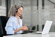 Smiling middle aged female support service employee talking to customer sitting at desk. Happy senior old woman professional call contact center agent wearing headset hybrid working in business office
