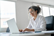 © insta_photos - Smiling senior professional woman looking at computer, happy middle aged female company executive, corporate manager using laptop technology hybrid working online in business office sitting at desk.