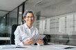 © insta_photos - Happy middle aged professional business woman using tab computer in office. Mature female bank manager, smiling older executive holding digital tablet looking at camera sitting at work desk. Portrait.