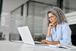© insta_photos - Busy mature business woman working in office using laptop. Middle aged old professional lady executive manager entrepreneur looking at computer thinking on digital technology strategy sitting at desk.
