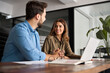 © insta_photos - Two happy colleagues man and woman talking at work. Smiling professional business people using laptop having conversation working in office discussing corporate strategy at workplace.