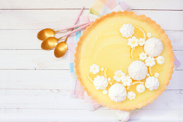 Poster - Spring lemon tart with white chocolate flowers and meringue. Easter dessert concept. Overhead view table scene over a white wood background.