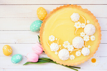 Poster - Spring lemon tart with white chocolate flowers and meringue. Easter dessert concept. Top view table scene over a white wood background.