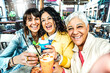 Three senior women friends drinking cocktail glasses sitting at bar table - Group of best friends enjoying happy hour cheering drinks at pub restaurant  - Life style concept with girls take a selfie