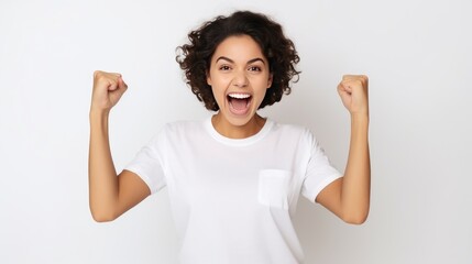 Happy cheerful girl with dark hair combed in bun clenches fist celebrates success holds smartphone dressed in casual basic t shirt jeans isolated over white wall receives message about reward.