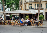 Fototapeta Paryż - Typical view of the Parisian street with tables of brasserie (cafe) in Paris, France. Cozy cityscape of Paris. Architecture and landmarks of Paris.