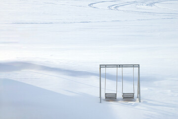 Wall Mural - Panoramic view of snowy desert with snowmobile tracks. Lonely snow-covered swings in the foreground. Copy space.