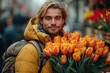 Handsome blond man in a yellow winter jacket with a bouquet of tulips in hands. flowers for international women's day. spring holidays concept