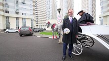 Man In Suit Is Standing Near Horse Carriage With A Coachman Outside.