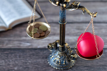 Balance scales with red heart shape and coins with holy bible book in the background. Selective focus. Christian priorities, justice, tithing, giving, love, or money concept.