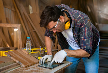 A young modern caucasian craftsman using tablet computer design woodcraft at the carpentry workshop