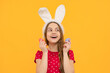 Teenager child wearing bunny ears and hold colorful painted easter eggs isolated at yellow background.