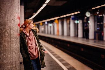 Wall Mural - Pensive Wait at Subway Station, Young woman leaning against a pillar, waiting at a subway station