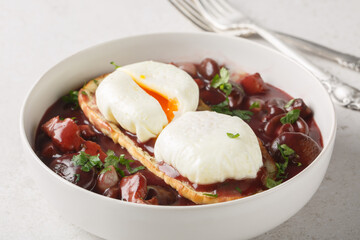 Oeufs en meurette is a classic French dish of poached eggs covered in a rich red wine sauce filled with lardons, mushrooms and onion closeup on the plate on the table. Horizontal