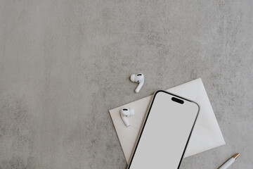 Blank screen mobile phone with copy space, wireless earphones on concrete background. Flat lay, top view. Copy space mockup template