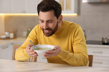 Wall Mural - Man enjoying delicious soup at light marble table in kitchen