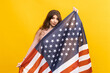 © makedonski2015 - The American flag takes center stage in this eye-catching photo, as a young woman holds it up against a bright yellow background