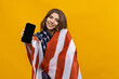 © makedonski2015 - A smiling woman with a flag on her shoulders holding a smartphone on a yellow background. Successful business in USA
