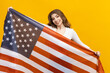© makedonski2015 - This photo features a young woman beaming with patriotism, as she holds up the American flag against a cheerful yellow background