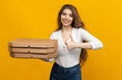 © makedonski2015 - A pizza delivery woman stands against a vibrant yellow backdrop, balancing several pizza boxes in her hands