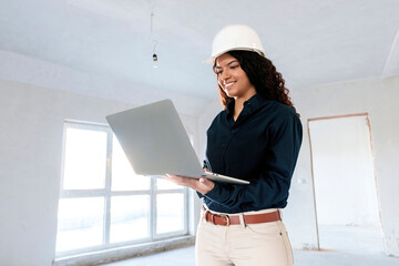 Happy architect wearing hardhat using laptop at site