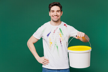 Poster - Young satisfied smiling employee laborer handyman man wear white stained t-shirt hold brush paint tin isolated on plain green background. Instruments for renovation apartment room Repair home concept