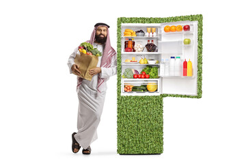 Canvas Print - Saudi arab man in ethnic clothes standing next to an eco-friendly green fridge