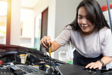 Wall Mural - Woman smiles while checking car engine oil. Woman checking car engine oil in the shade working.